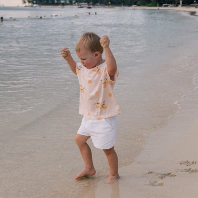 Child playing on a beach wearing apricot t-shirt