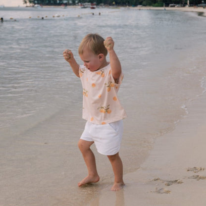 Child playing on a beach wearing apricot t-shirt