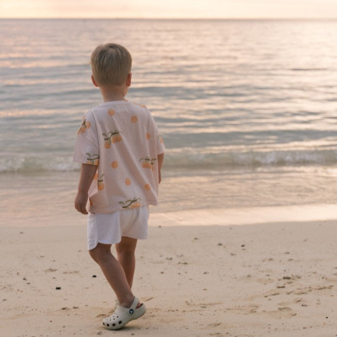 Child standing on a beach looking at the ocean during sunset wearing apricot t-shirt