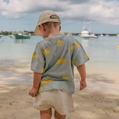 Child standing on a beach looking at the water with boats in the background