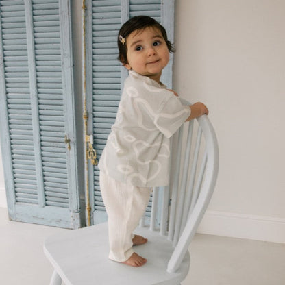 Child in a white pear t-shirt standing on a white chair with light blue shutters in the background