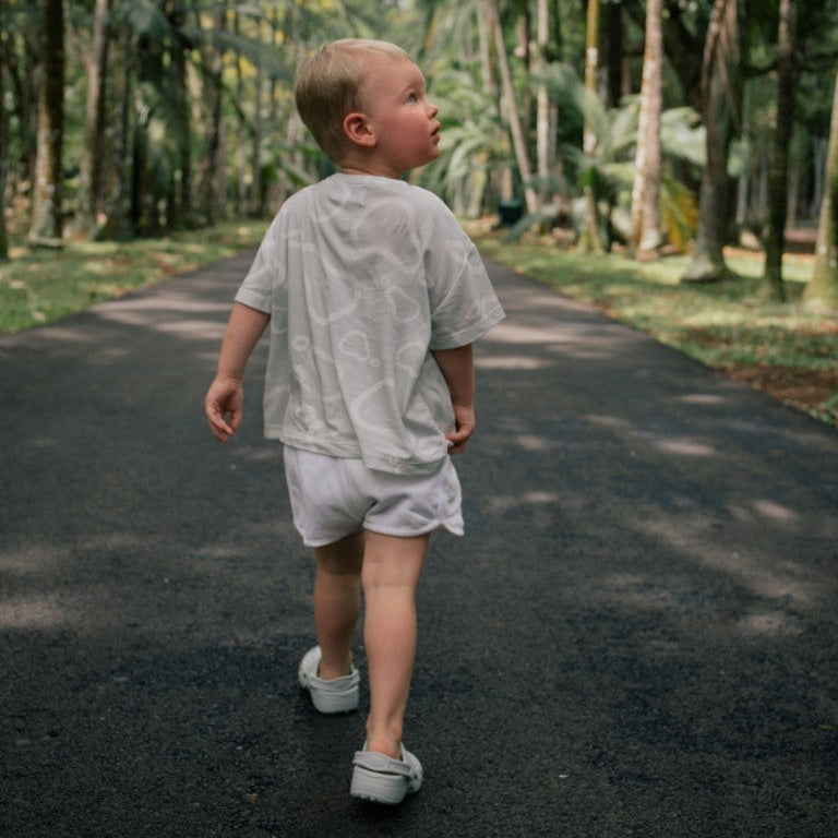 Child walking on a path in a forest with white pear t-shirt on