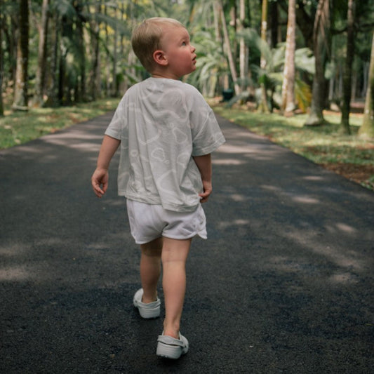 Child walking on a path in a forest with white pear t-shirt on