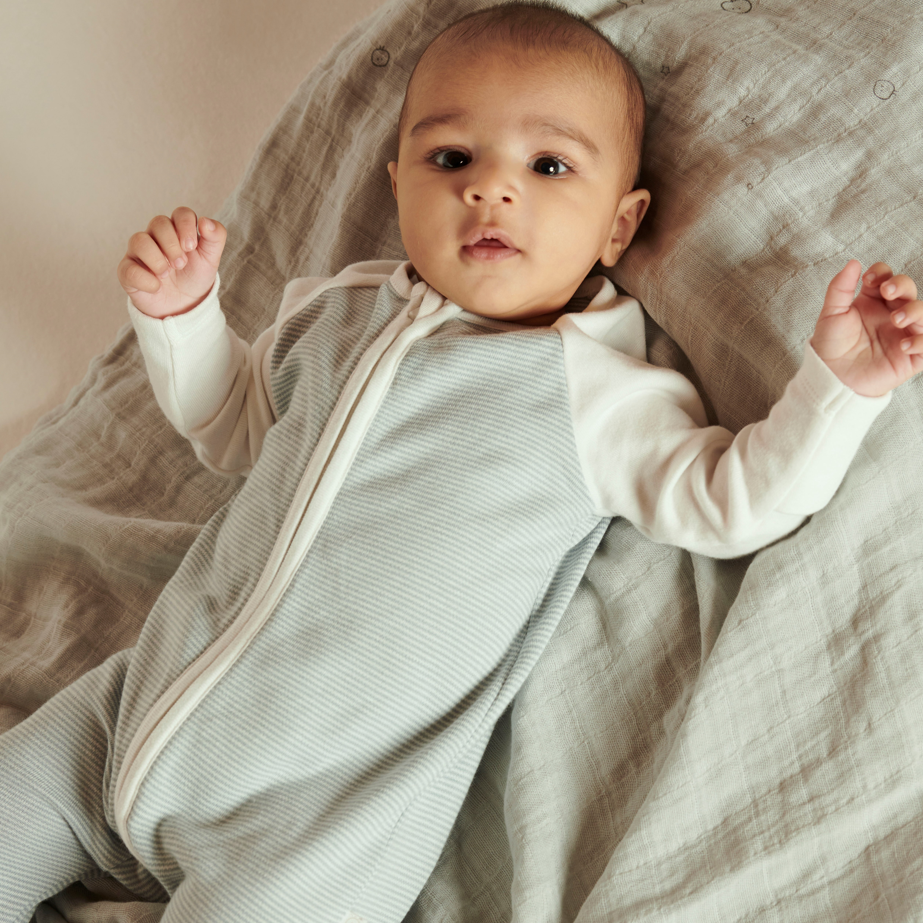 Baby wearing blue stripe sleepsuit with white raglan sleeves